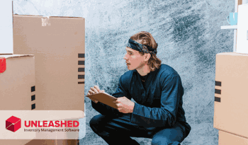 man crouching looking at boxes and writing notes onto a clipboard